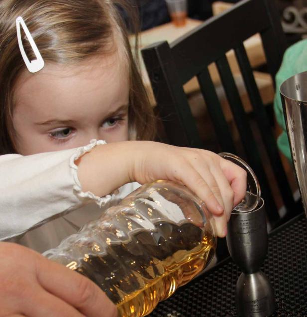 Ein junges Mädchen gießt eine gelbe Flüssigkeit aus einer Flasche in einen Messbecher.