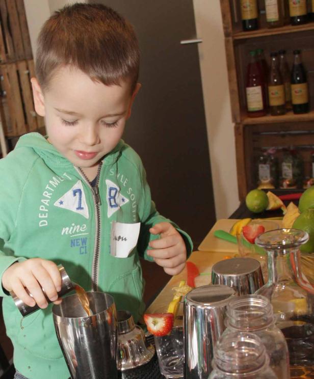 Ein kleiner Junge mixt einen Cocktail hinter einer Bar.
