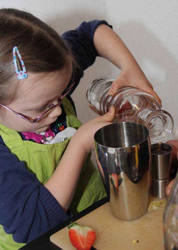 Ein junges Mädchen gießt Flüssigkeit aus einer Glasflasche in einen Cocktailshaker.