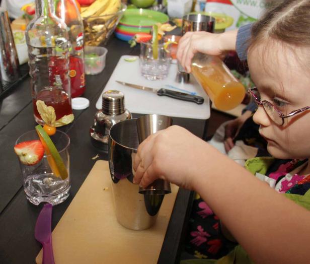 Ein junges Mädchen mixt einen Cocktail mit Früchten in einer Küche.