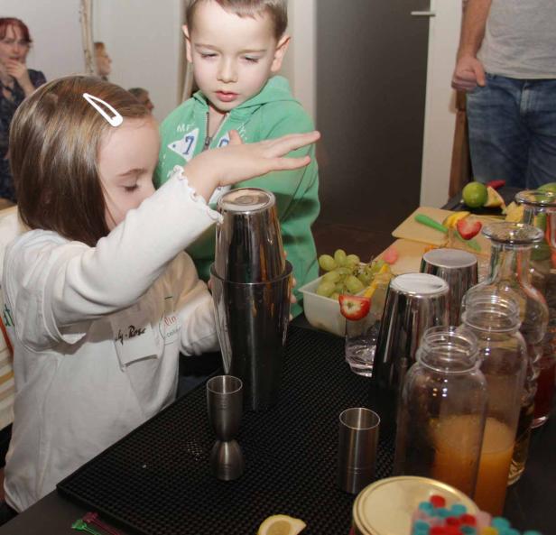 Ein Mädchen mixt mit einem Cocktailshaker, während ein Junge zusieht.