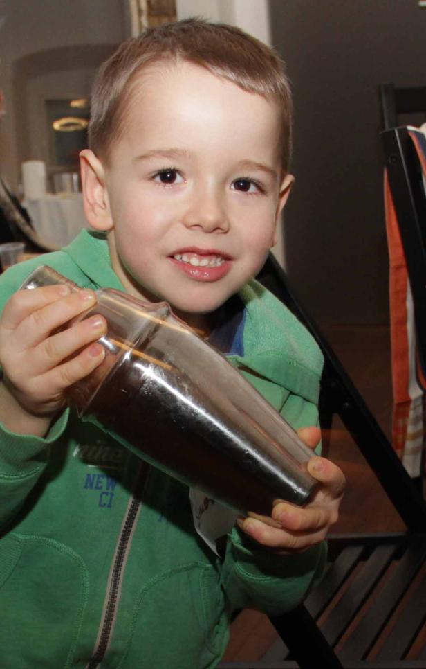 Ein lächelnder Junge hält einen Cocktailshaker in seinen Händen.