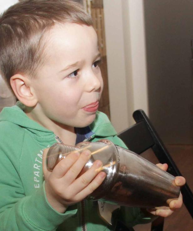 Ein kleiner Junge hält einen Cocktailshaker fest in seinen Händen.