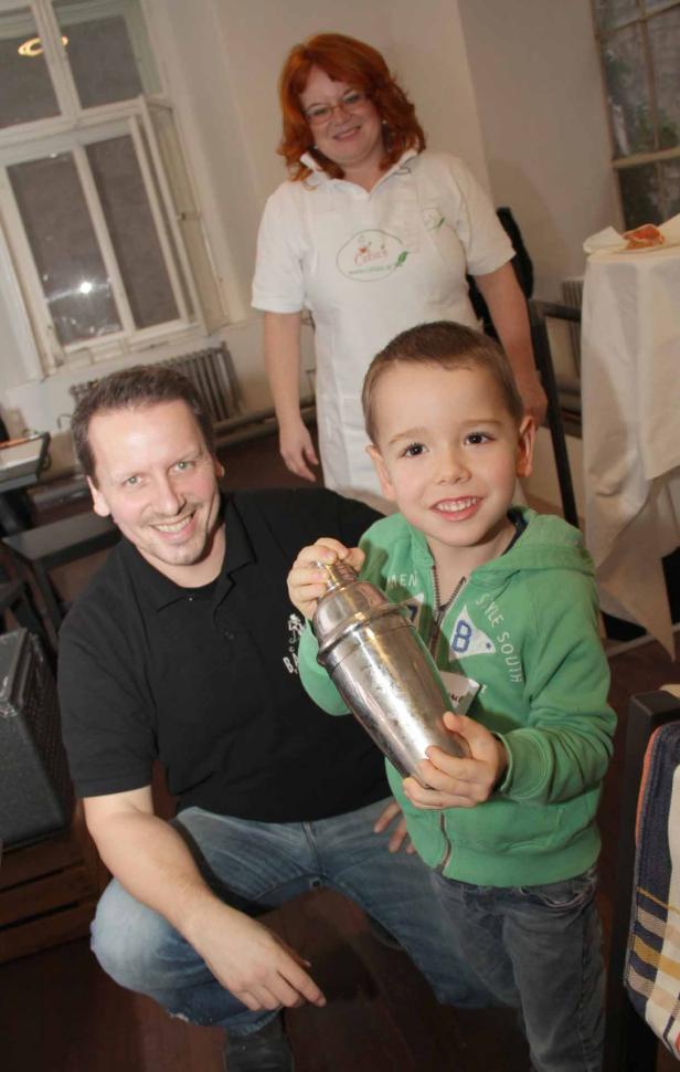 Ein Junge hält einen Cocktailshaker, während ein Mann und eine Frau lächeln.