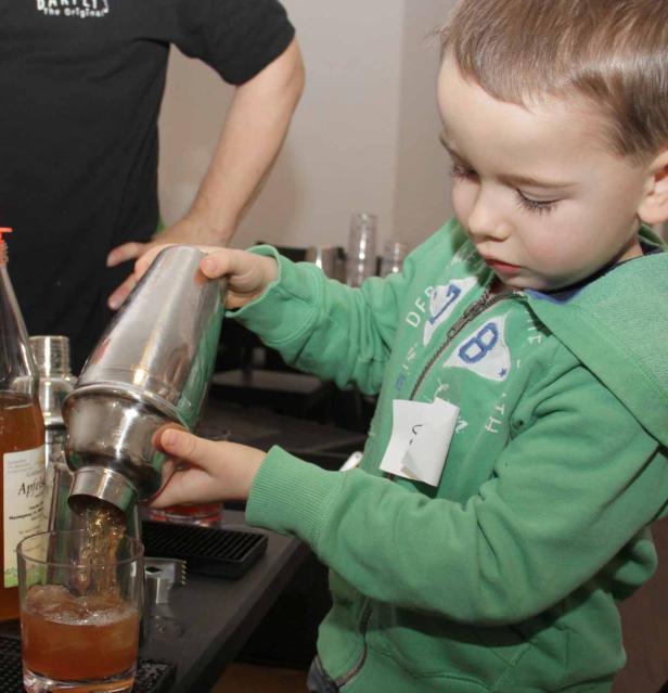 Ein kleiner Junge gießt ein Getränk aus einem Shaker in ein Glas.