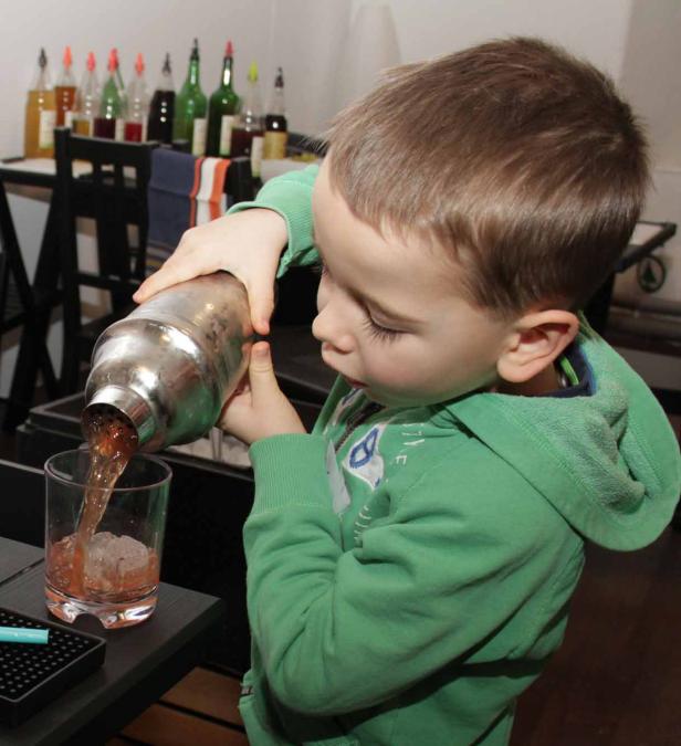 Ein Junge gießt ein Getränk aus einem Shaker in ein Glas mit Eiswürfeln.