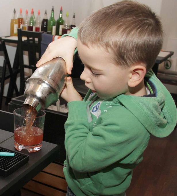 Ein Junge gießt ein Getränk aus einem Shaker in ein Glas.