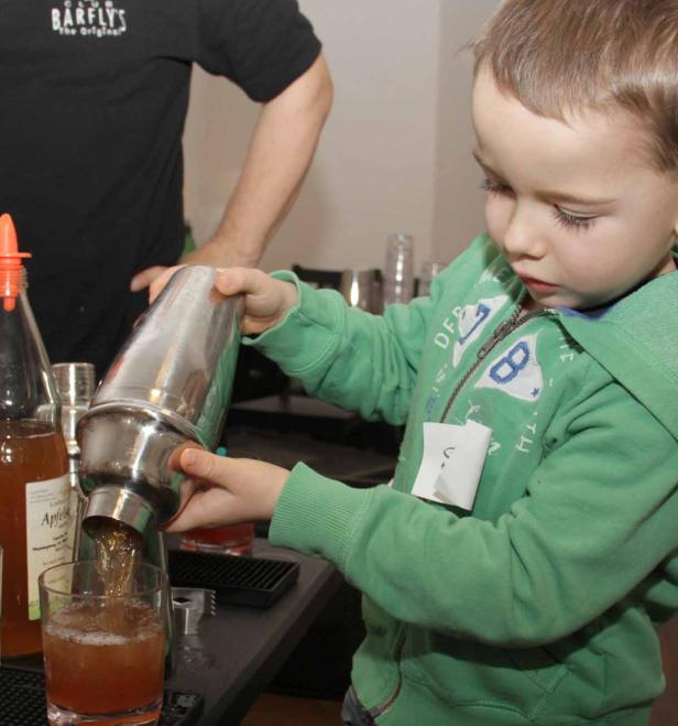 Ein kleiner Junge mixt mit einem Cocktailshaker ein Getränk in ein Glas.