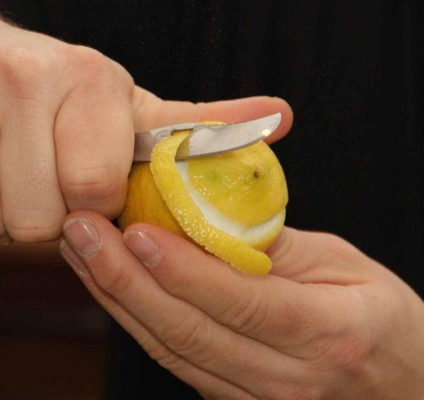 Eine Person schält mit einem Messer die Schale einer Zitrone.