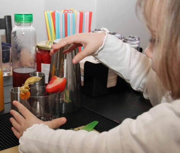 Ein Kind dekoriert ein Getränk mit einer Erdbeere und einer Physalis.