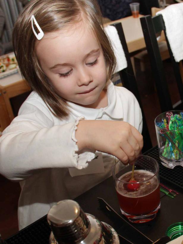 Ein kleines Mädchen legt eine Cocktailkirsche in ein Getränk.