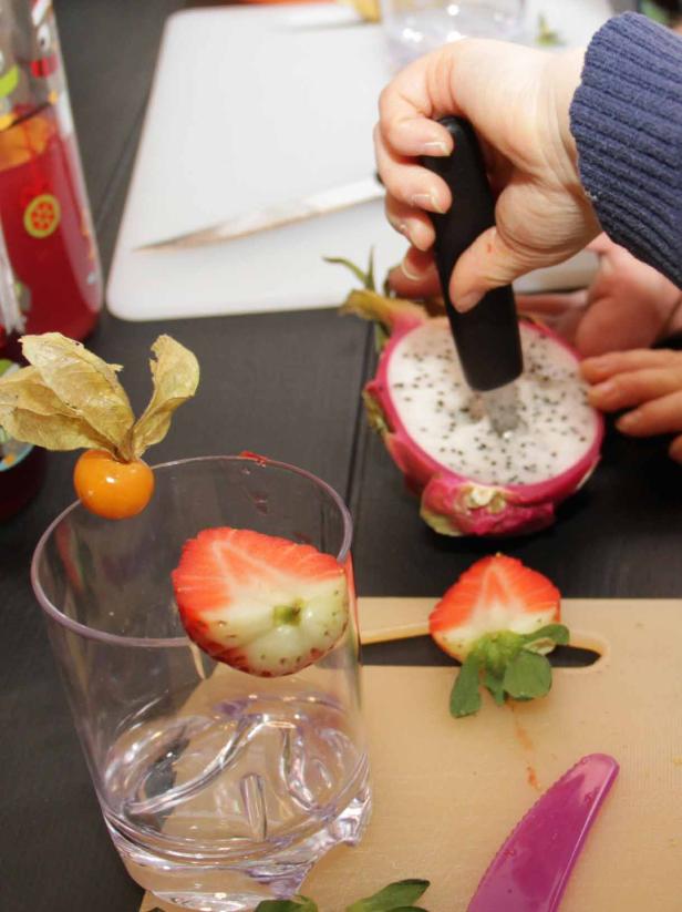 Eine Person bereitet einen Cocktail mit Erdbeeren, Physalis und Drachenfrucht zu.