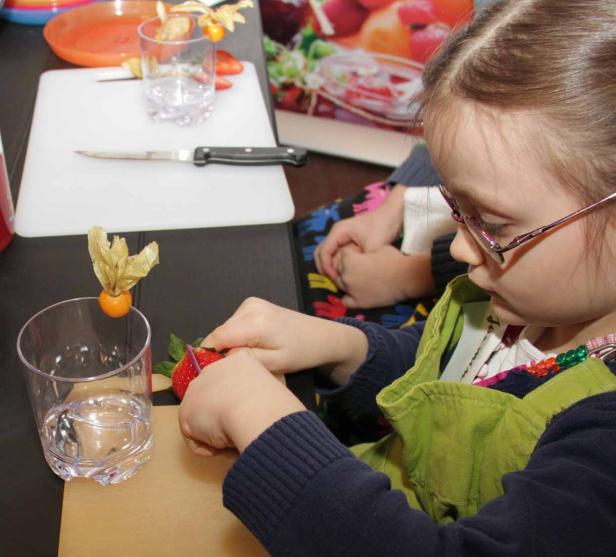 Ein Mädchen mit Brille schneidet Erdbeeren für einen Nachtisch zu.