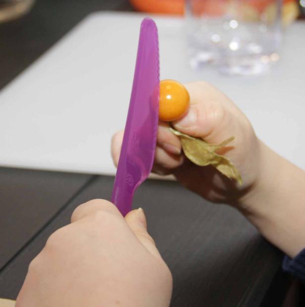 Eine Person schneidet mit einem lila Messer eine Physalis.