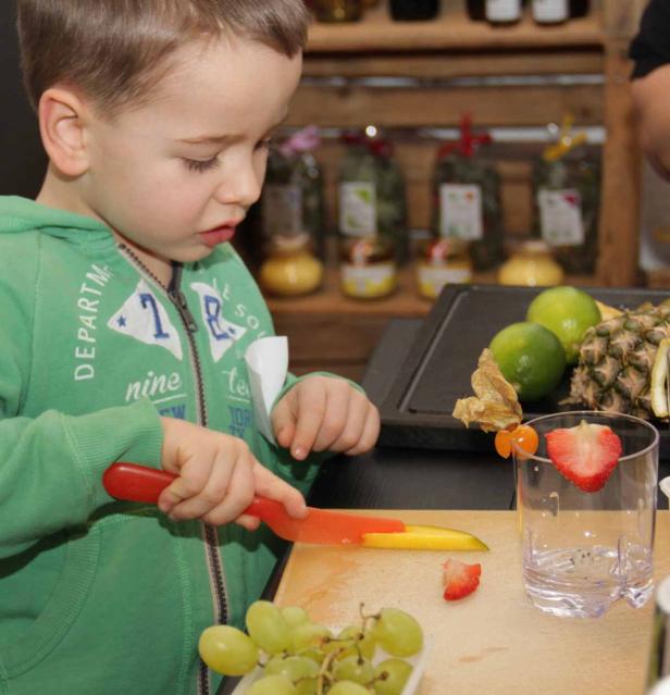 Ein kleiner Junge schneidet mit einem Messer eine Mango auf einem Schneidebrett.