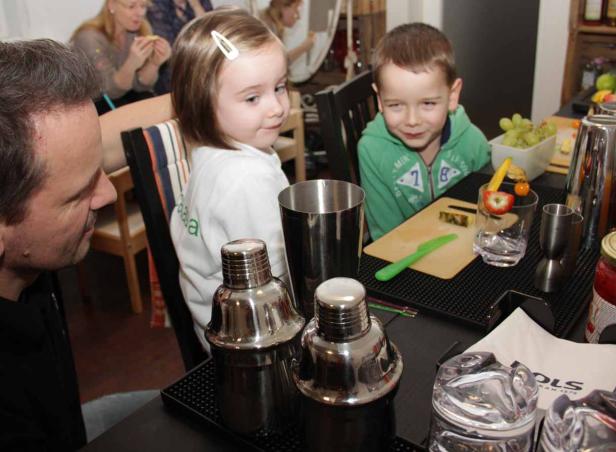 Ein Mann und zwei Kinder stehen an einer Bar mit Cocktail-Zutaten.
