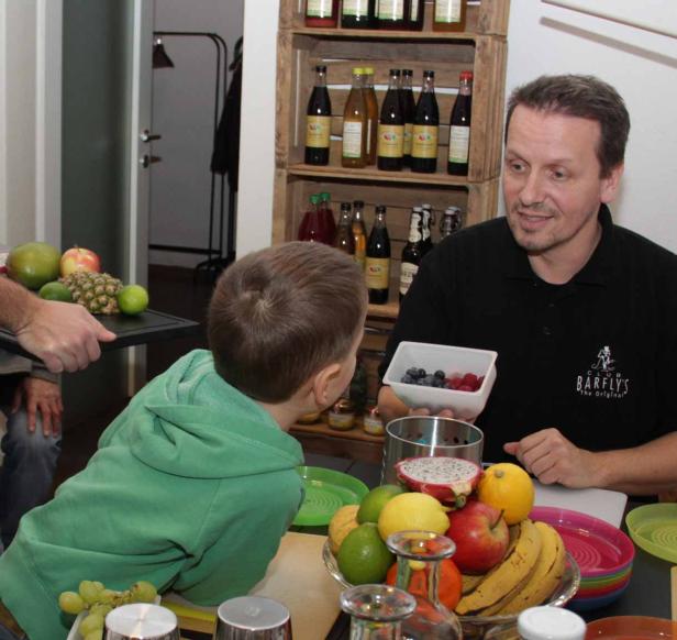 Ein Mann von „Bärflys“ zeigt einem Kind frische Beeren vor einem Tisch voller Früchte.