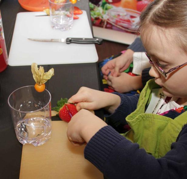 Ein Mädchen schneidet Erdbeeren für einen Cocktail zu.