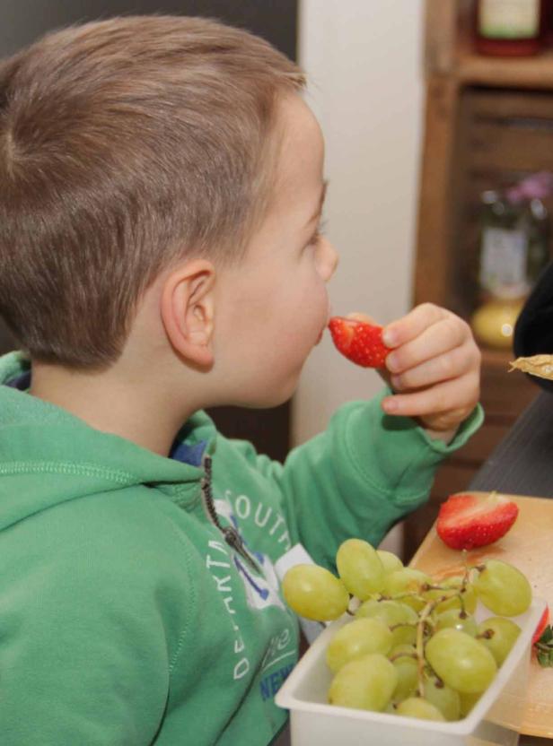Ein Junge isst eine Erdbeere, neben ihm eine Schale mit Weintrauben.