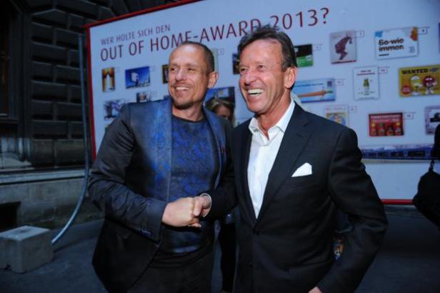 Zwei Männer schütteln sich die Hände vor einer Werbetafel für den Out of Home-Award 2013.