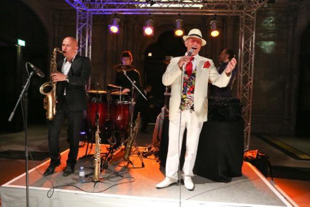 Eine Band spielt live auf einer Bühne mit Saxophon, Schlagzeug und Gesang.