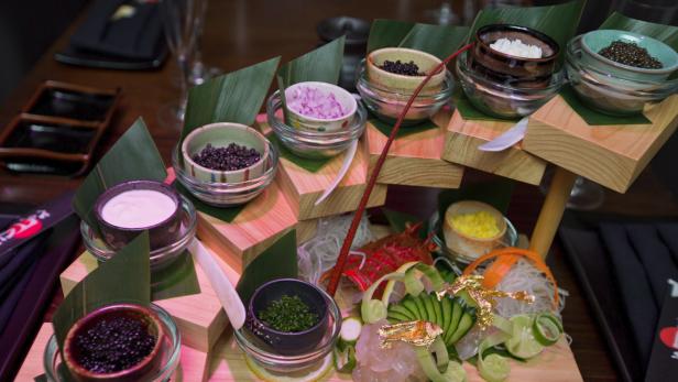 Eine kunstvolle Präsentation von Kaviar, Dips und Beilagen auf einem Holztablett.