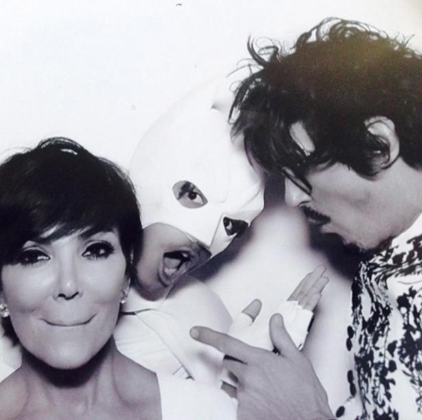 Kris Jenner posiert mit zwei Personen, von denen eine eine weiße Maske trägt.