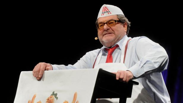 Ein Mann mit Kochmütze und Schürze steht an einem Pult mit einer Zeichnung von Gemüse.