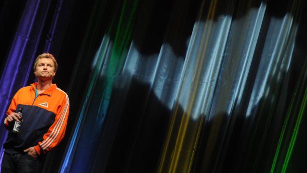 Ein Mann mit Jacke hält eine Flasche in der Hand vor einem farbig beleuchteten Hintergrund.