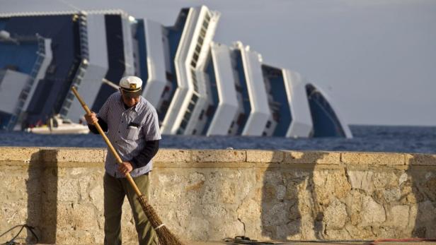 EPAepa03066850 A man sweeps the pavement backdropped by the cruise ship Costa Concordia that ran aground off the coast of Giglio Island, Italy, 19 January 2012. Italian rescue service divers on 19 January resumed their search aboard the half-sunken Costa EPAepa03066850 A man sweeps the pavement backdropped by the cruise ship Costa Concordia that ran aground off the coast of Giglio Island, Italy, 19 January 2012. Italian rescue service divers on 19 January resumed their search aboard the half-sunken Costa