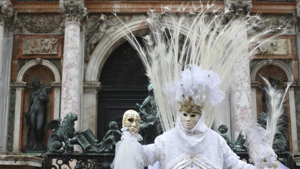 Eine Person in einem weißen Karnevalskostüm mit Federn und einer Maske in Venedig.