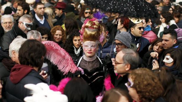 Eine verkleidete Frau mit Federboa steht inmitten einer Menschenmenge beim Karneval in Venedig.