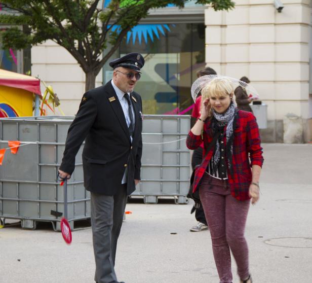 Ein Mann in Uniform und eine Frau mit karierter Jacke gehen auf der Straße.