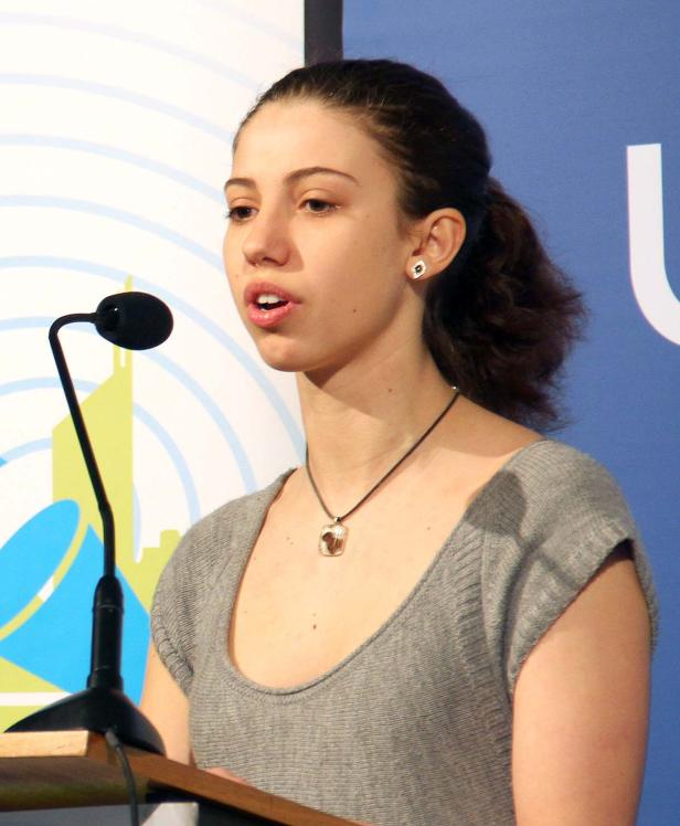 Eine junge Frau spricht an einem Rednerpult vor einem Mikrofon.