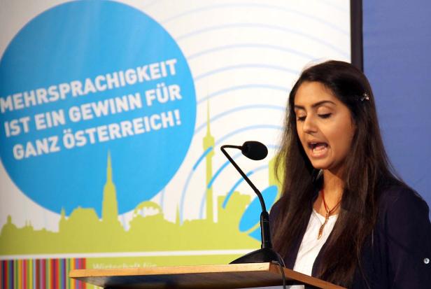 Eine Frau spricht bei einer Veranstaltung vor einem Banner über Mehrsprachigkeit.