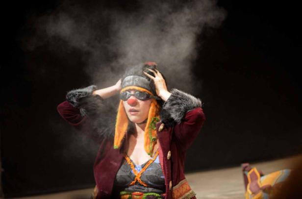 Eine Person mit Clown-Make-up und Brille steht im Rampenlicht.