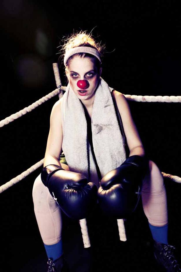 Eine Boxerin mit Clownsnase sitzt erschöpft im Ring.