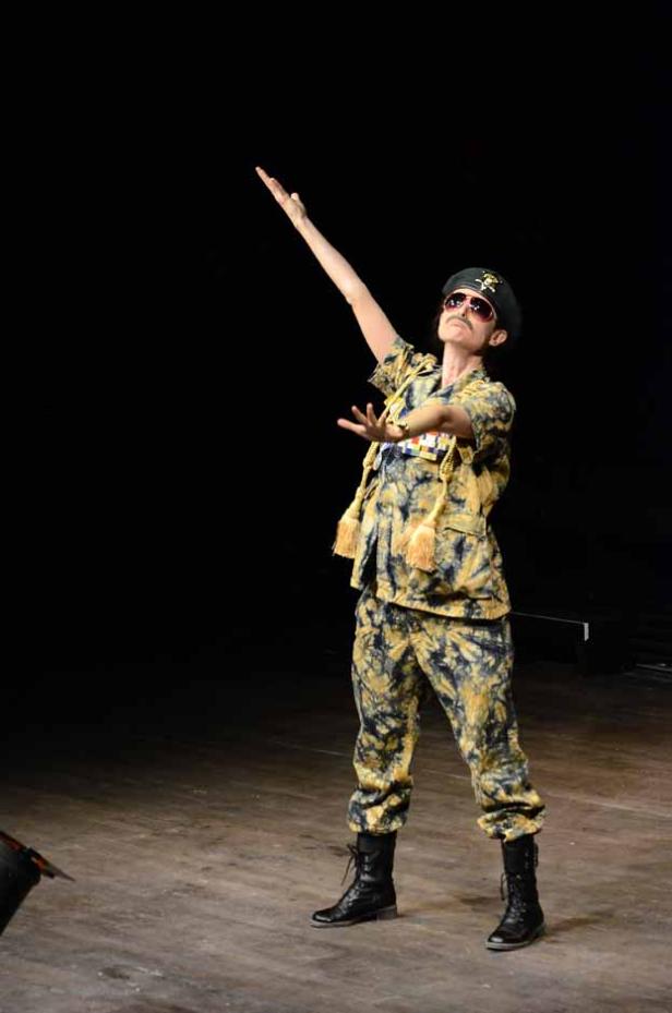 Eine Person in Militäruniform und Sonnenbrille posiert auf einer Bühne.