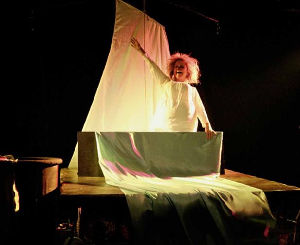 Eine Frau in einem weißen Kleid steht auf einer Bühne vor einem Segel.