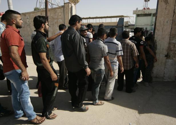 Eine Menschenmenge steht an einer staubigen Straße an einer Wand Schlange.