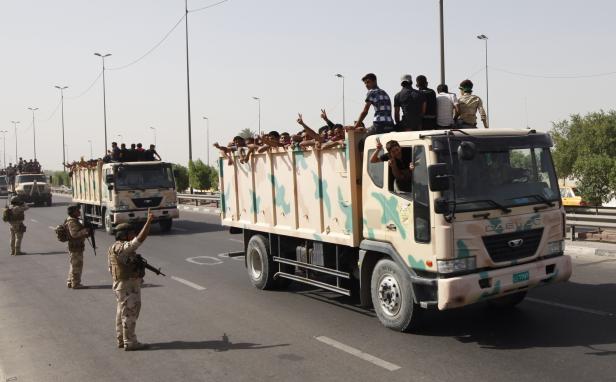 Soldaten eskortieren Lastwagen voller Menschen auf einer Straße.