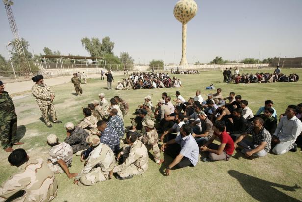 Eine große Gruppe von Männern sitzt auf einem Rasen unter einem getarnten Wasserturm.