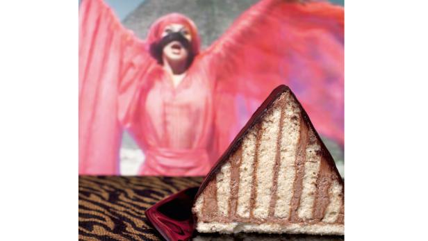 Ein Stück Schokoladentorte vor einem unscharfen Hintergrund mit einer Person in einem roten Kostüm.