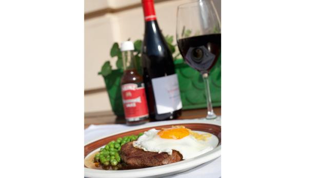 Ein Teller mit Steak, Spiegelei und Erbsen, dazu eine Flasche Wein und Soße.