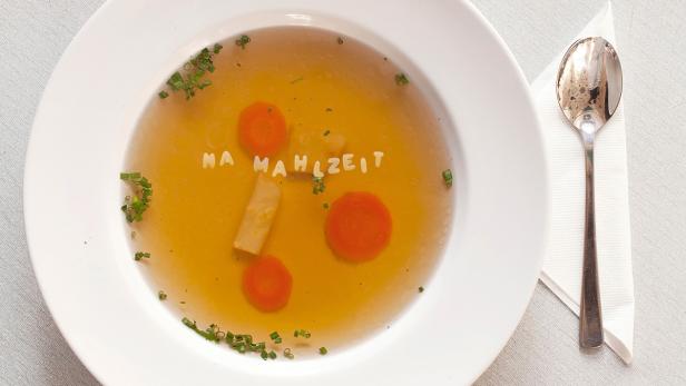 Eine klare Suppe mit Karotten, Lauch und Nudeln in Buchstabenform, die „Na Mahlzeit“ ergeben.