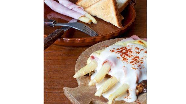 Spargel mit Schinken und Sauce Hollandaise auf einem Holzbrett angerichtet.