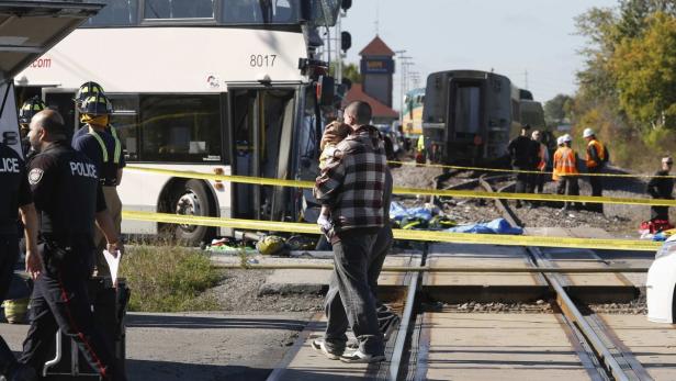 Ein Mann trägt ein Kind über Bahngleise an der Unfallstelle eines Busses und eines Zuges.