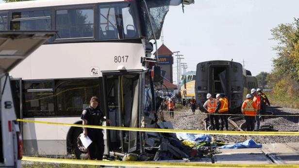Ein Bus und ein Zug sind in einen Unfall verwickelt, umgeben von Absperrband und Rettungskräften.