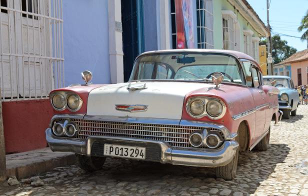 Ein rot-weißer Oldtimer steht auf einer Kopfsteinpflasterstraße in Kuba.