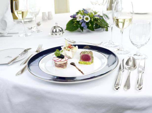 Ein Teller mit drei verschiedenen, kunstvoll angerichteten Speisen auf einem gedeckten Tisch.